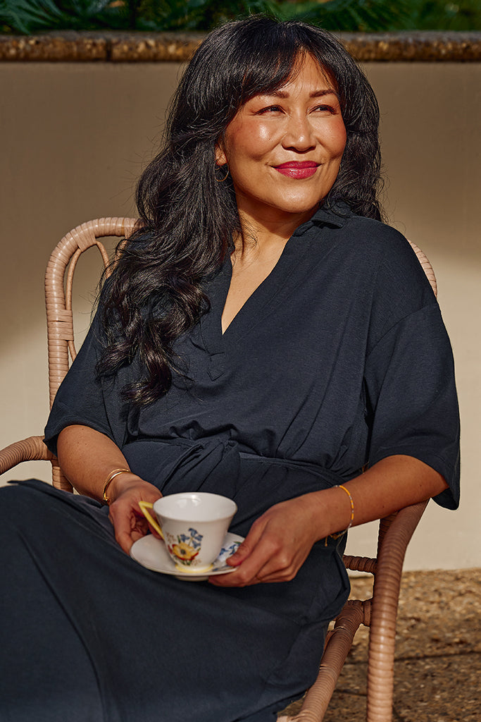 Close up of model sitting down in a relaxed posture wearing a bamboo-linen maxi dress in navy.