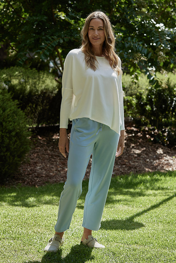 a woman wearing aquamarine pants with side pockets with a white asymmetric top
