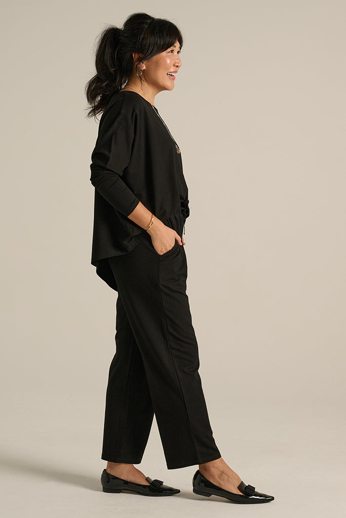 A model wearing black straight-leg trousers with an elasticated waistband and side pockets, paired with a matching black top.