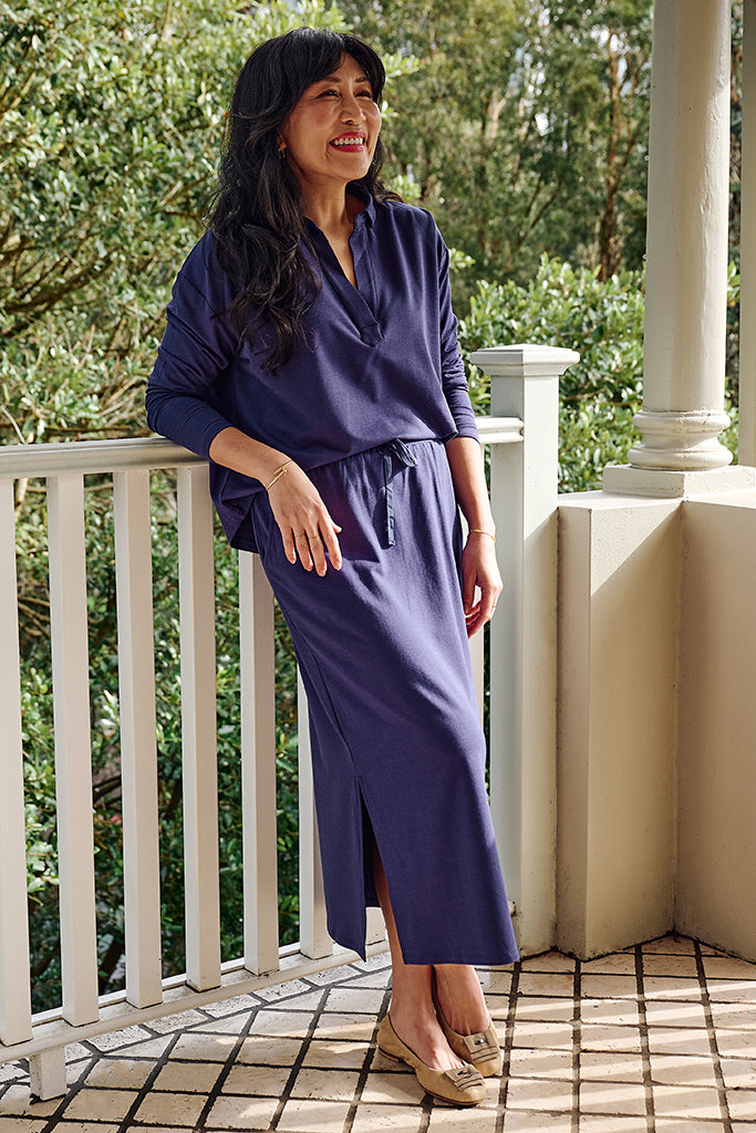 Woman in a purple bamboo set leaning on a balcony with greenery in the background