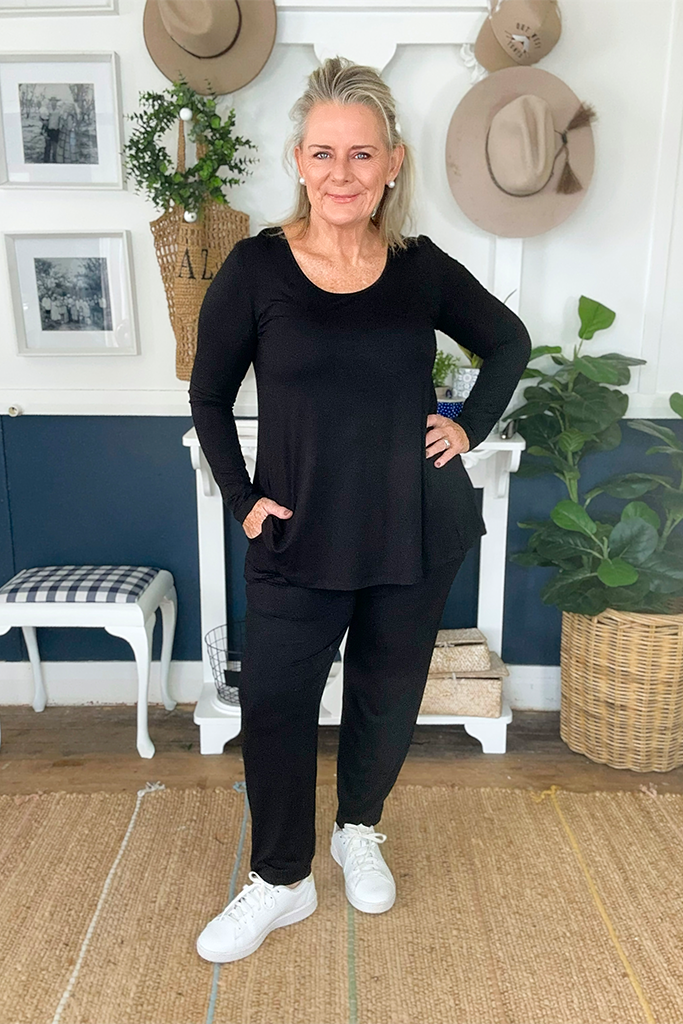 A woman wearing black bamboo trousers with an elastic waistband and tapered leg, paired with a relaxed black top and white sneakers.