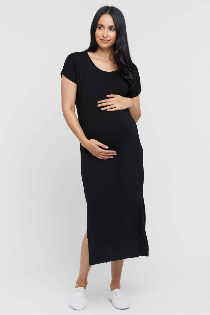 A pregnant woman wearing a black, maxi maternity dress with a round neckline, short sleeves, and side splits.