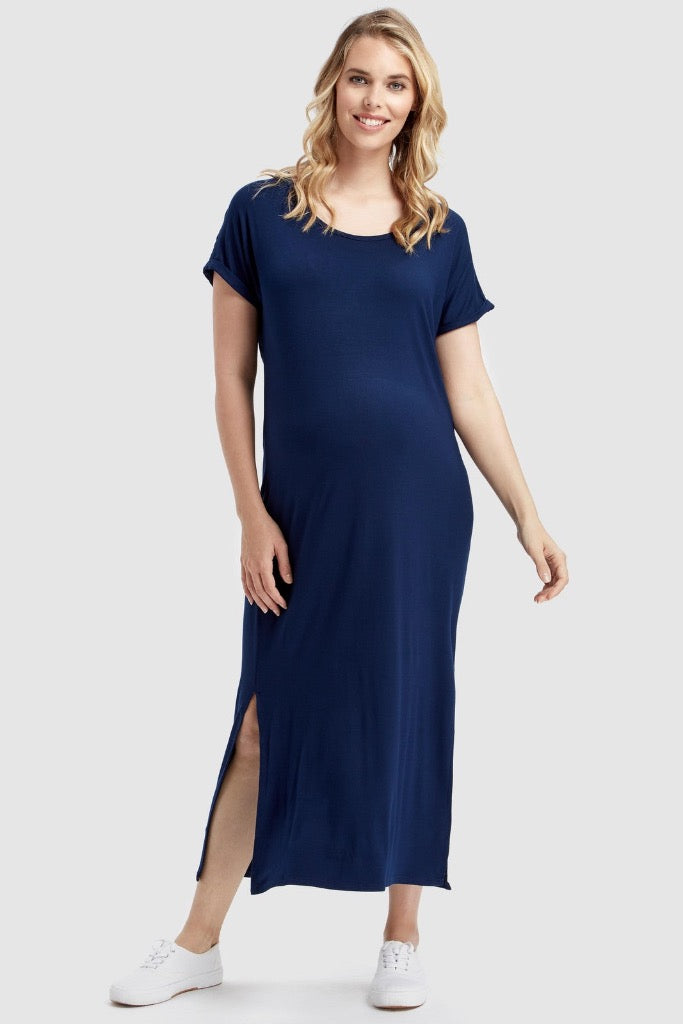 A pregnant woman wearing a navy maxi dress with a round neckline, short sleeves, and side splits, standing and smiling.