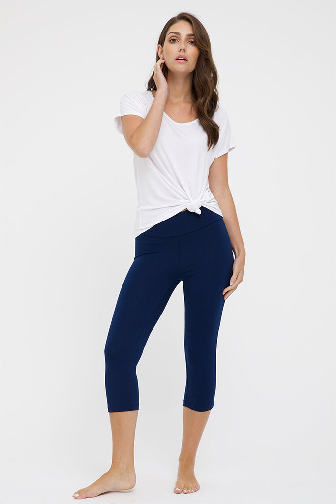 A woman standing and posing in navy 3/4 leggings and a white t-shirt