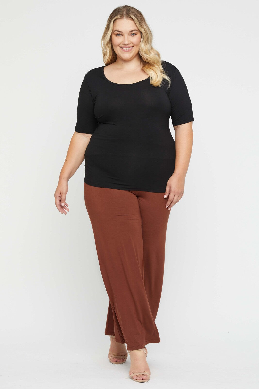 Curvy model wearing a body hugging black tee paired with rust coloured wide leg pants.