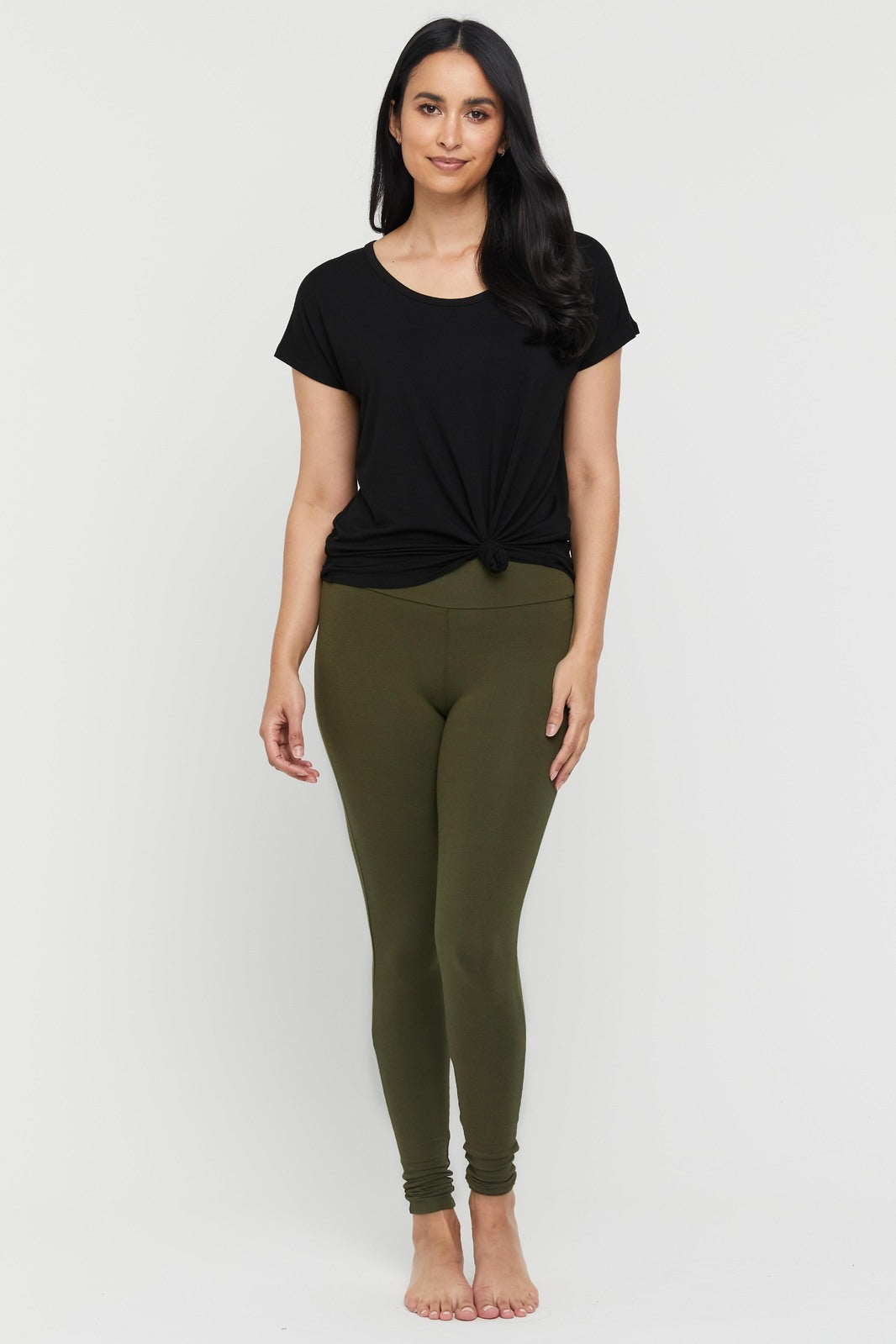 A woman wearing dark olive green high-waisted full-length leggings with a wide fabric waistband