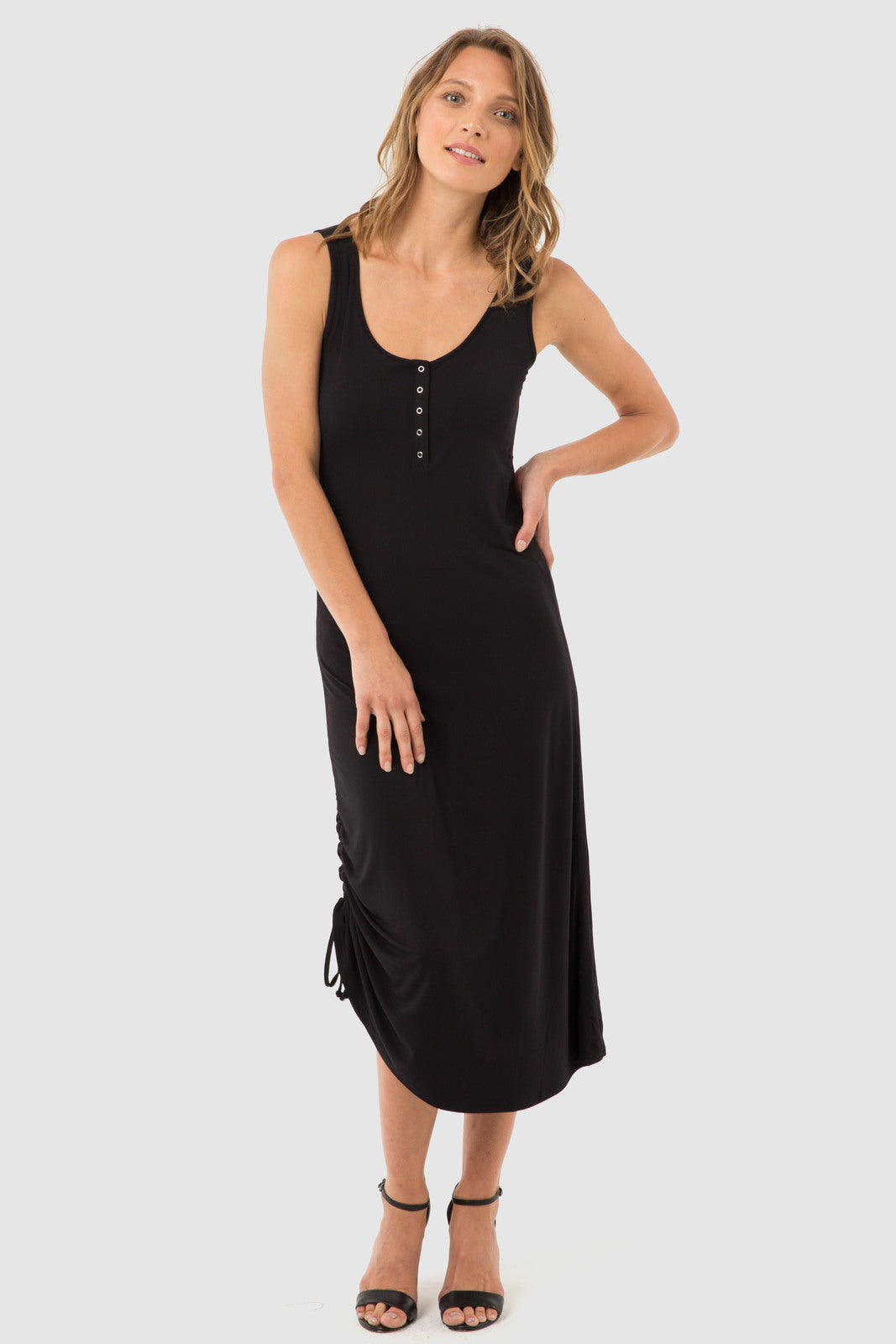 A model wearing a sleeveless, midi length black dress with a henley neckline and small buttons down the front.