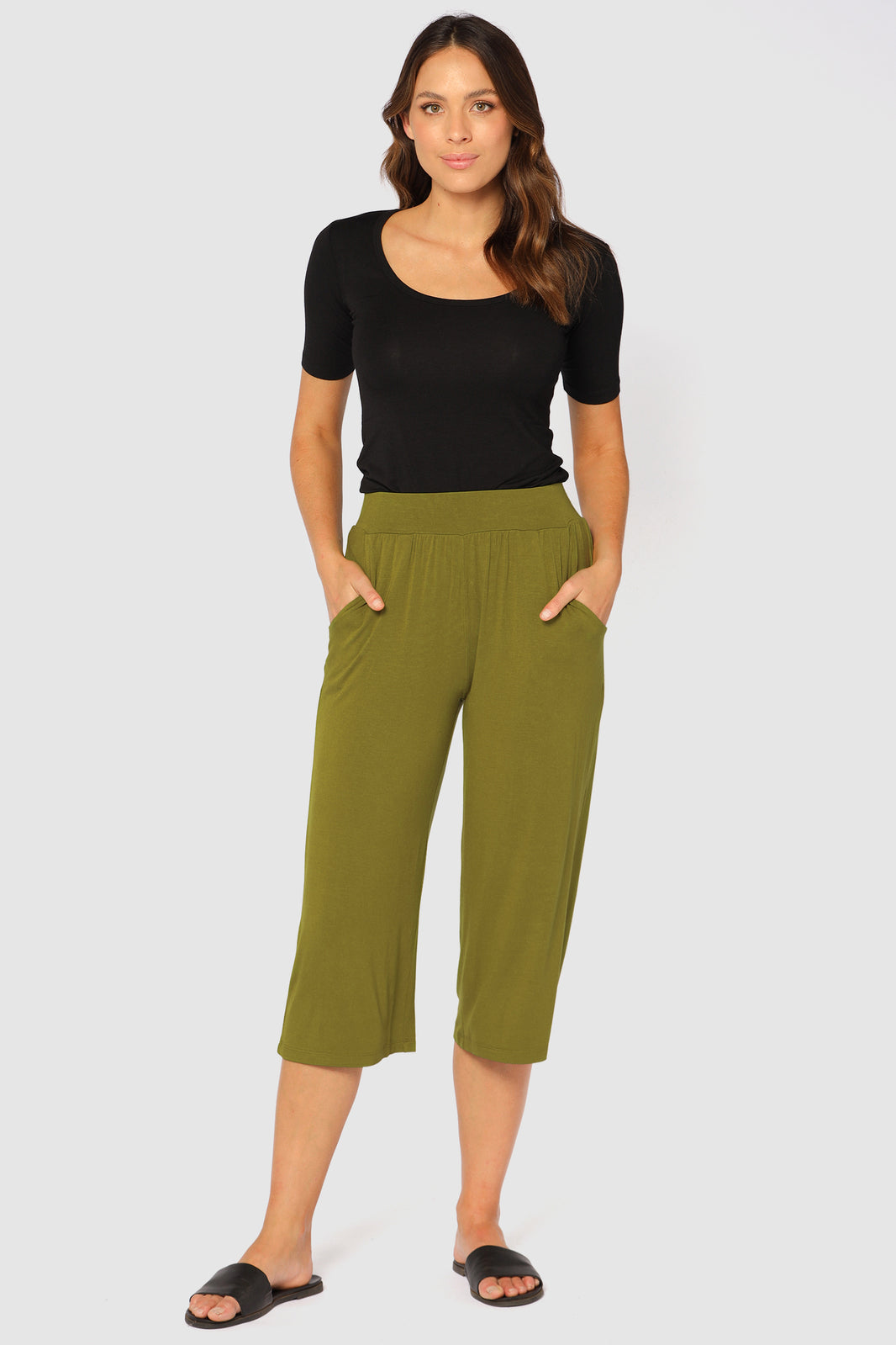 Model wearing a snug black bamboo tee with short sleeves paired with green pocket culottes and slides.