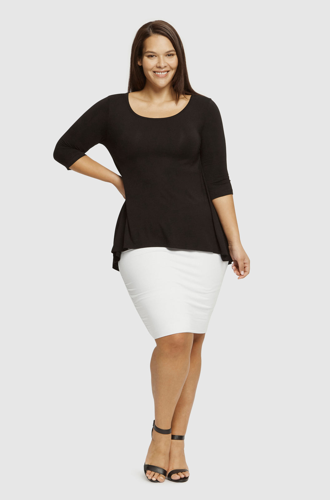 Plus size model wearing a relaxed black bamboo tee paired with a white tube skirt and black heels.