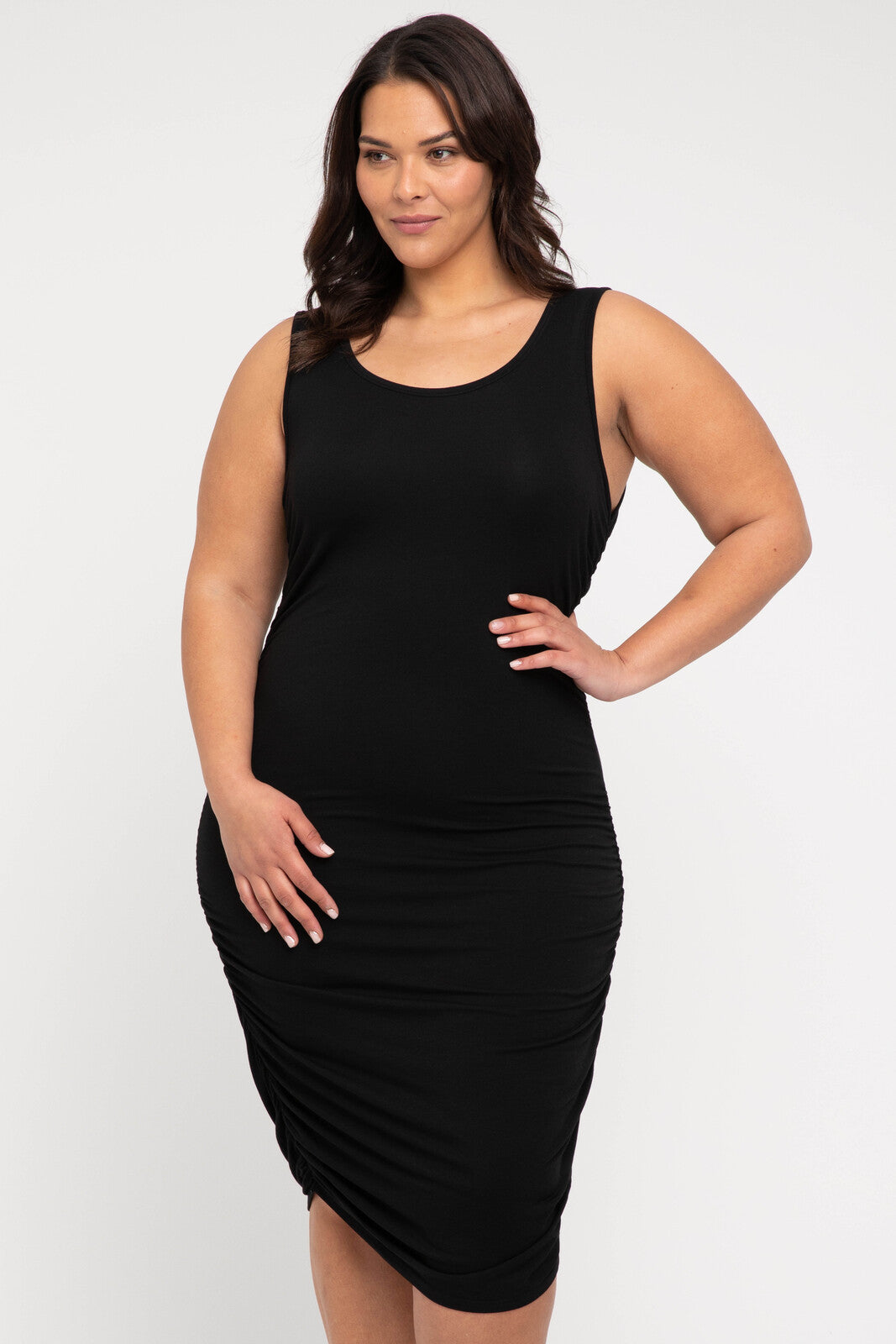 A model wearing a sleeveless, black, ruched tank dress with a scoop neckline and midi length.