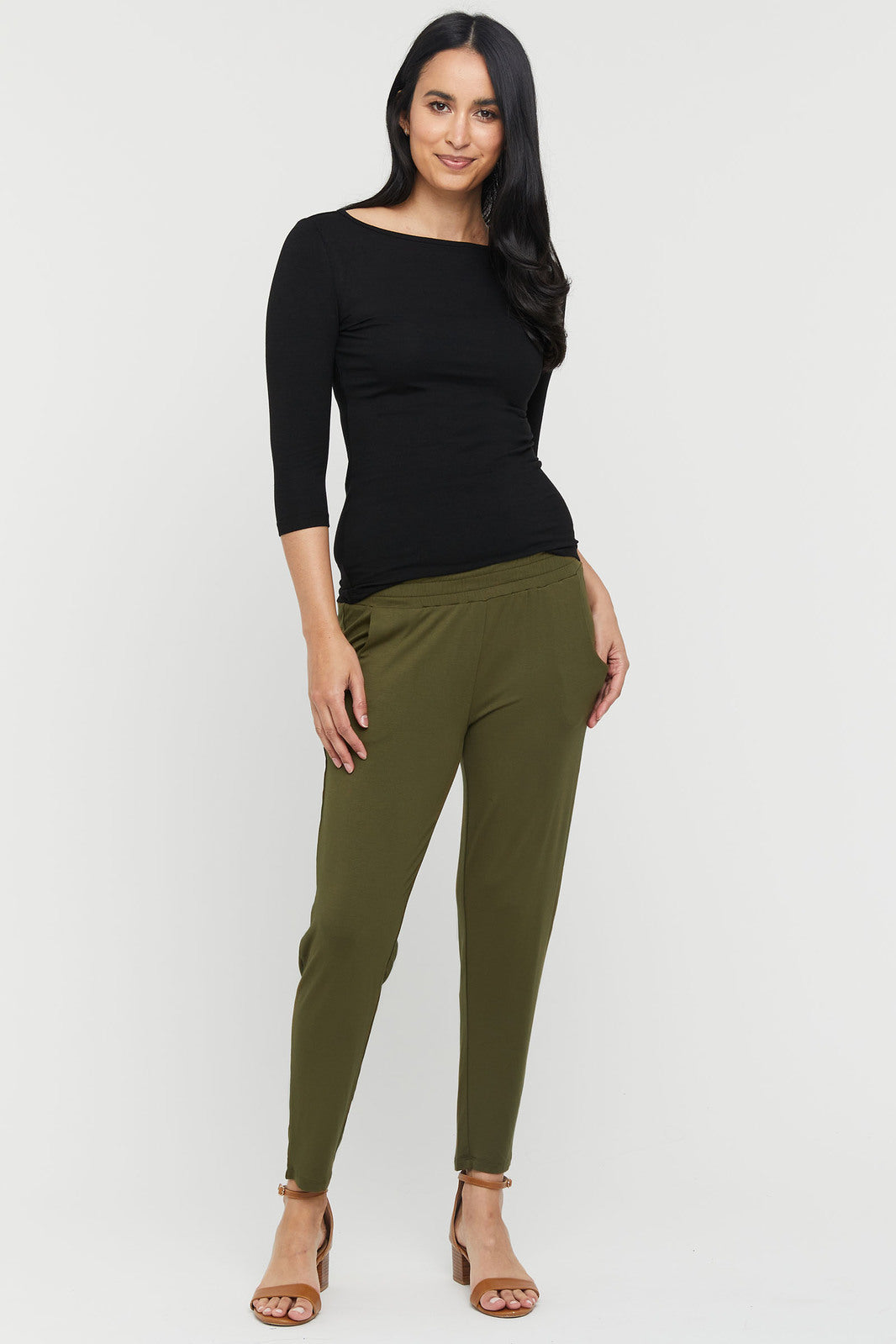 A woman wearing dark olive pants with an elasticated waistband, side pockets, and a tapered leg.