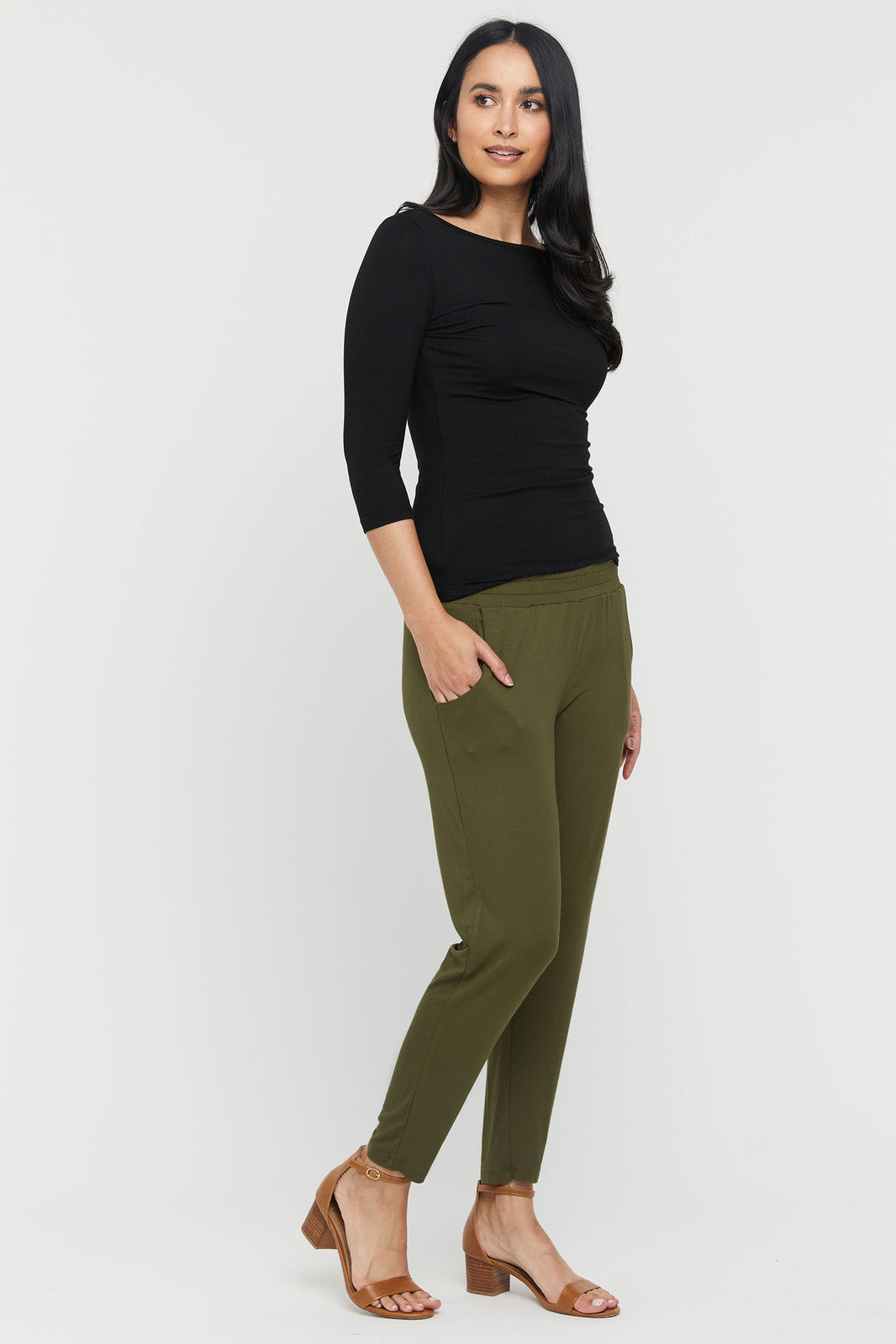 A woman wearing dark olive pants with an elasticated waistband, side pockets, and a tapered leg.
