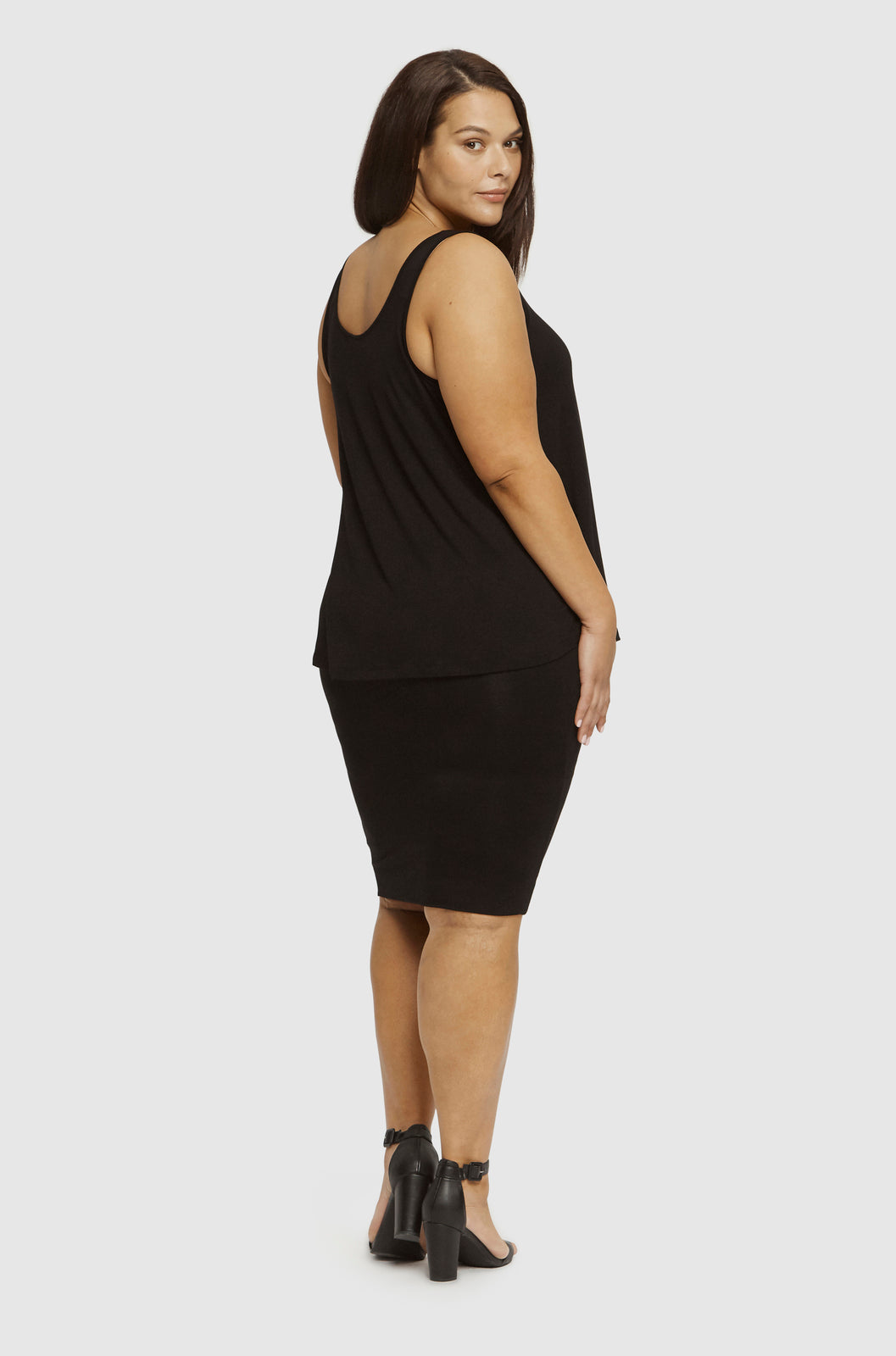 Plus size model in black singlet and black skirt standing back to camera looking over her shoulder