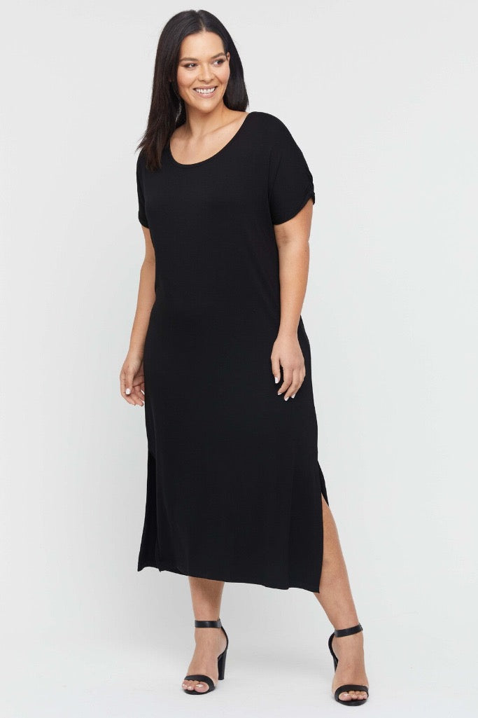 A model wearing a plus size black maxi dress with a scoop neckline, short sleeves, and side splits, paired with heels.