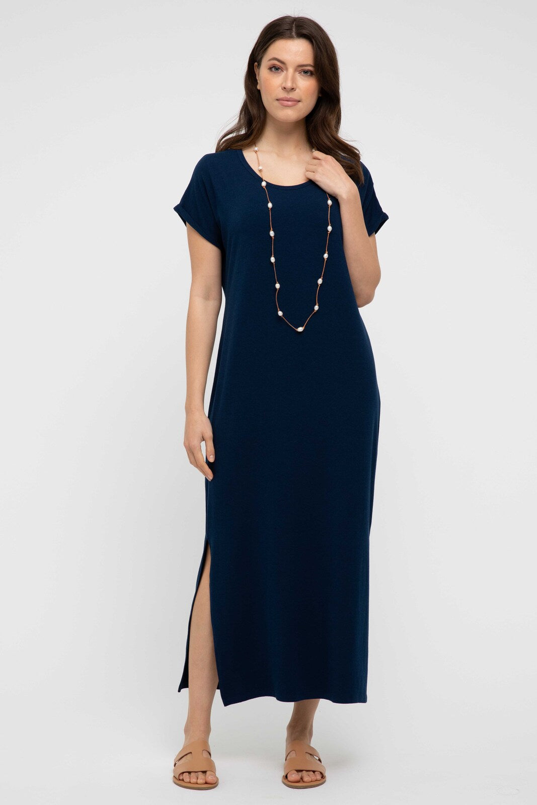 A navy maxi dress with a scoop neckline, short sleeves, and side splits to the knee. The dress is worn by a model who is accessorized with a necklace.