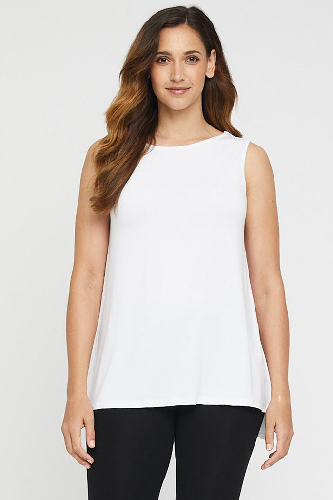 A woman wearing a white sleeveless top with a round neckline, the top has side slits and is longer at the back. She is paired with black leggings.