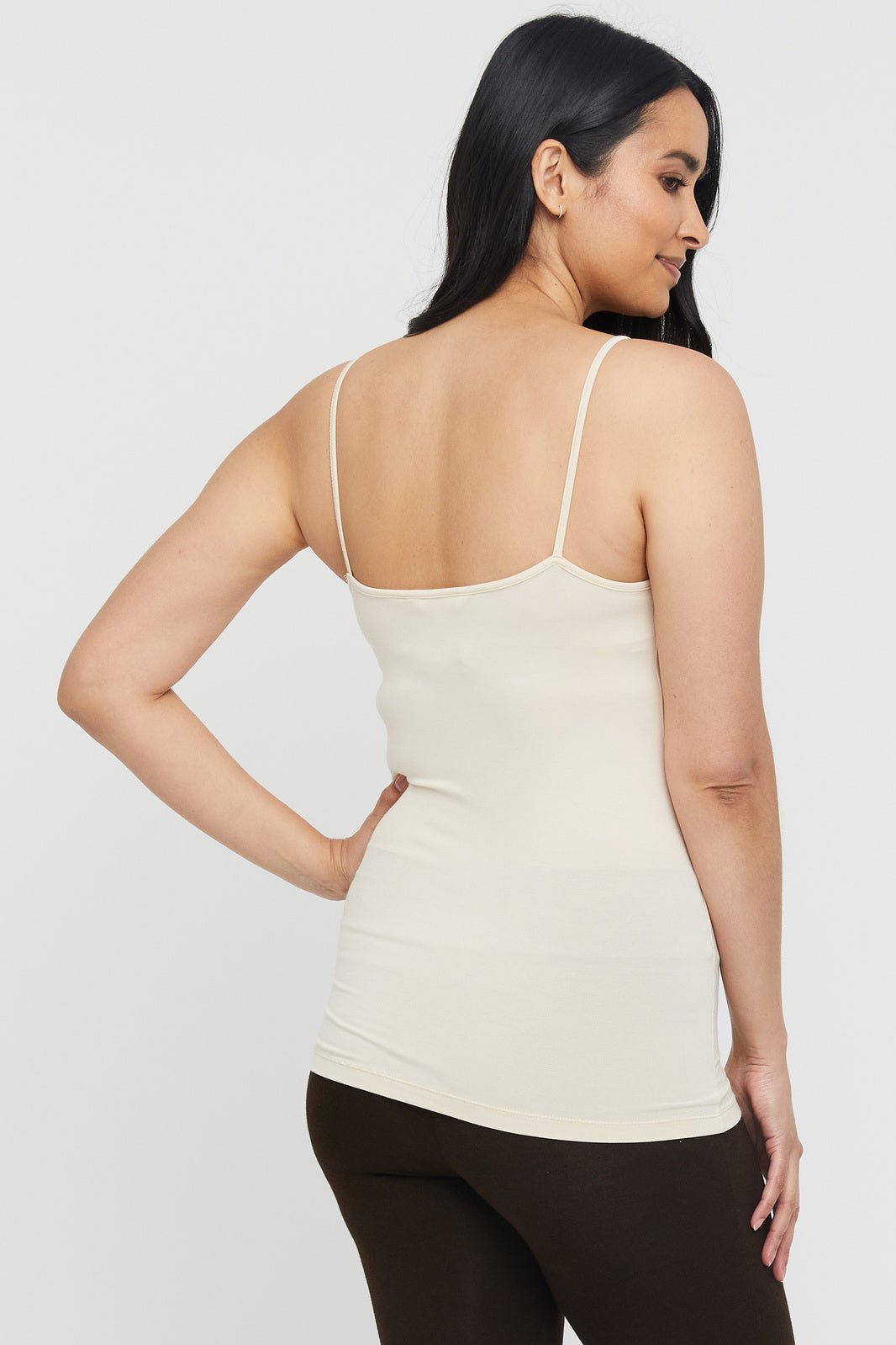 Showing the back of a model wearing a creme coloured camisole and brown leggings.