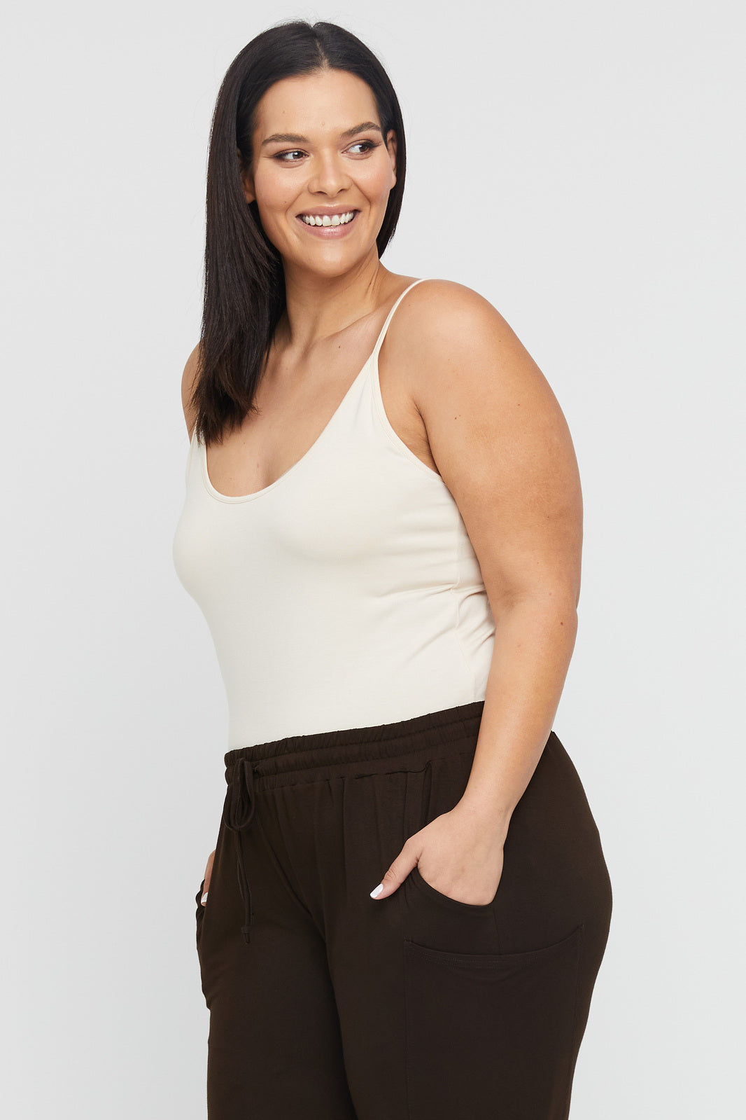 Plus size model wearing snug fitted ecru coloured cami with low scoop neck and thin shoulder straps.
