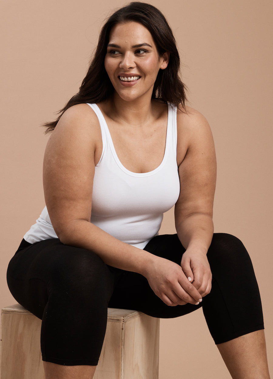 Plus size model sitting wearing white fitted singlet top