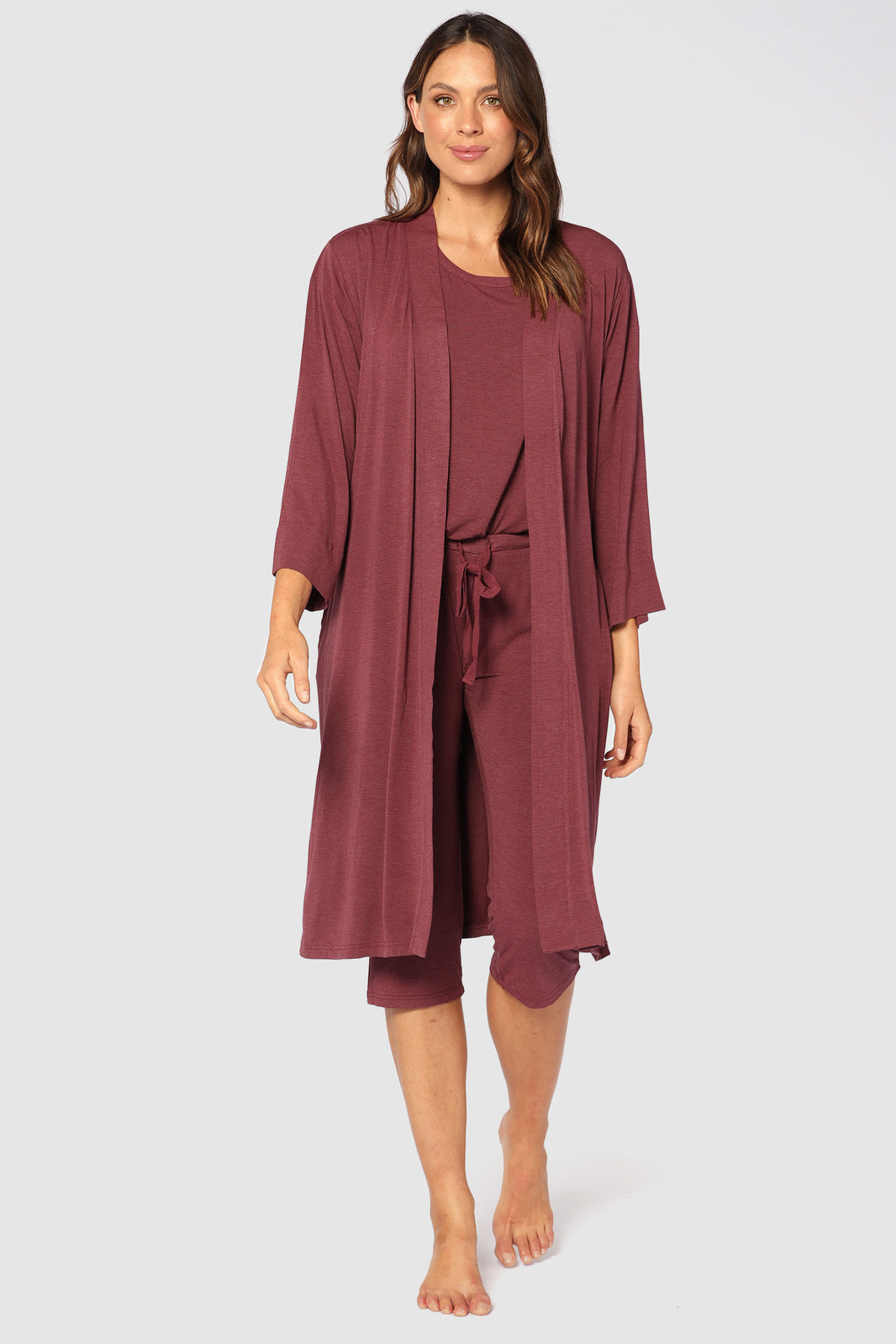 A woman wearing a burgundy sleepwear robe with wide sleeves, side pockets, and a tie around the waist. The robe is lightweight and made of a bamboo-cotton blend fabric.