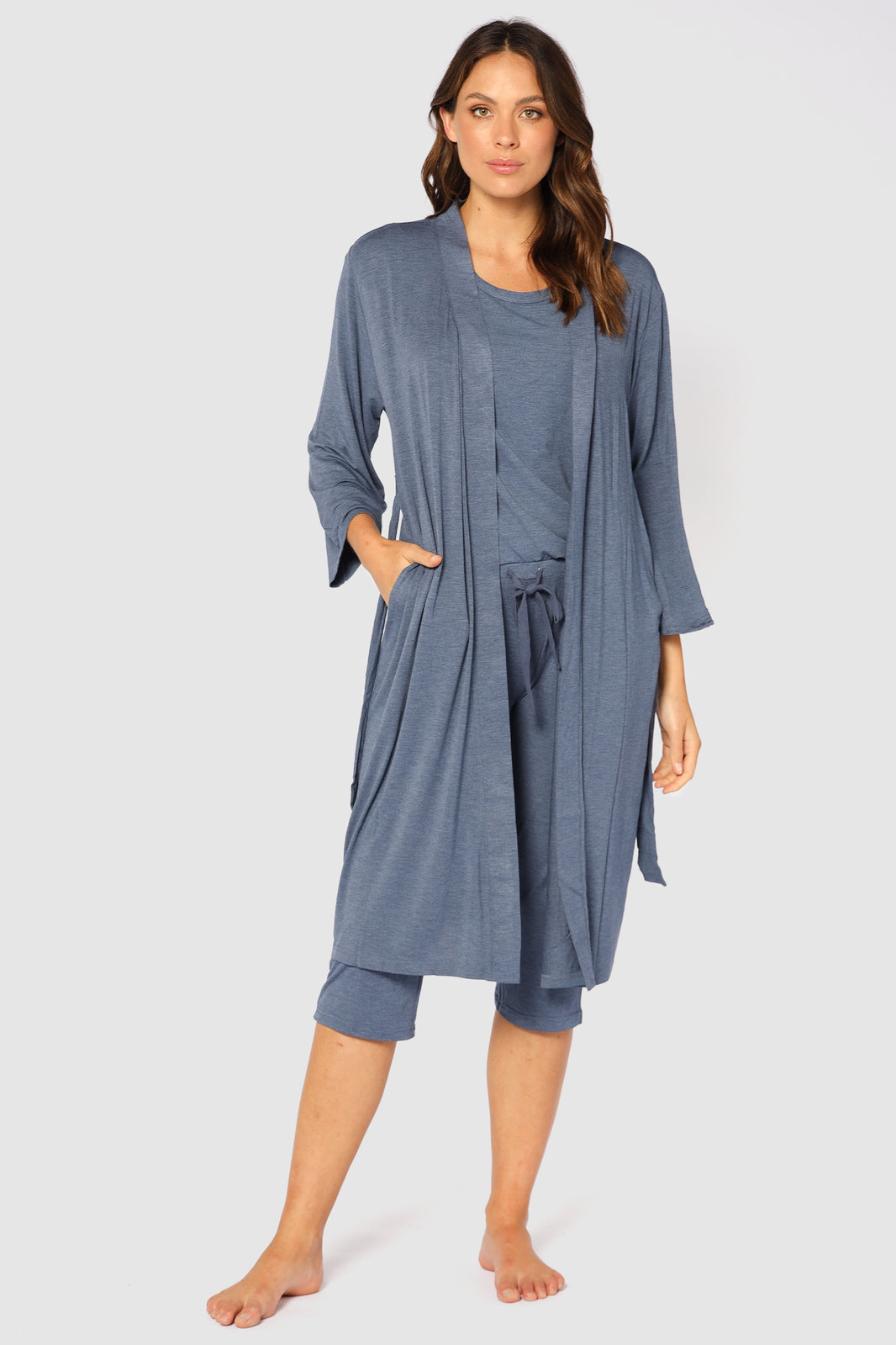 A female model wearing a blue sleepwear robe with wide sleeves, a tie waist, and side pockets, paired with matching 3/4 pants.