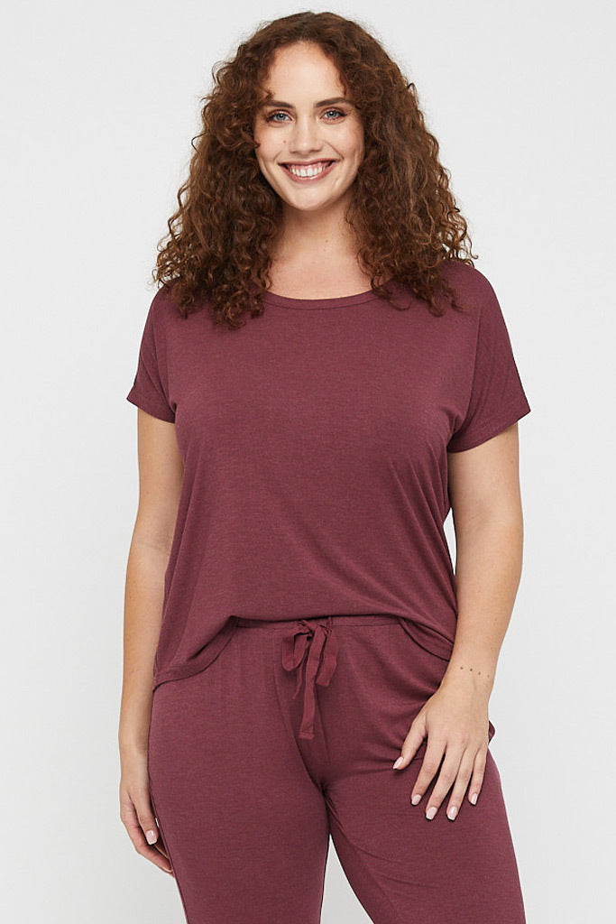 Plus size model wearing an oversized, relaxed tee in burgundy, featuring short sleeves and a round neckline.