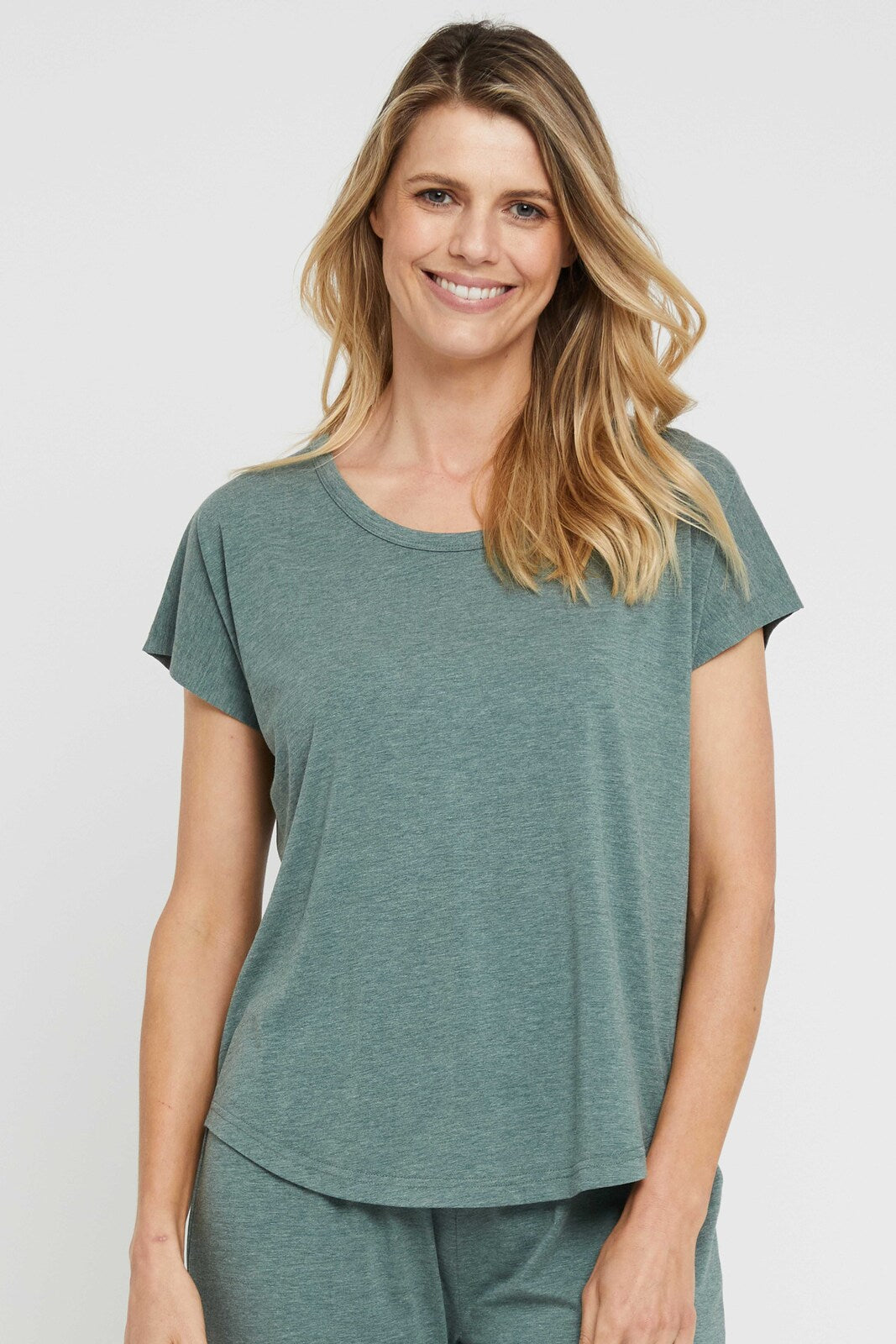 A woman wearing a moss green lounge tee with a round neckline, short sleeves, and a curved hemline, paired with matching pyjama pants.