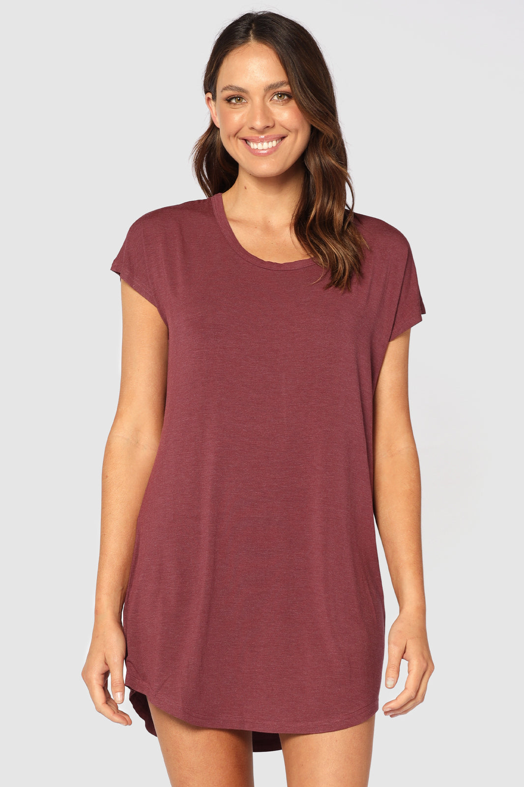 A woman wearing a burgundy bamboo night dress with a scoop neckline, short sleeves, and an oversized fit that falls above knee length.