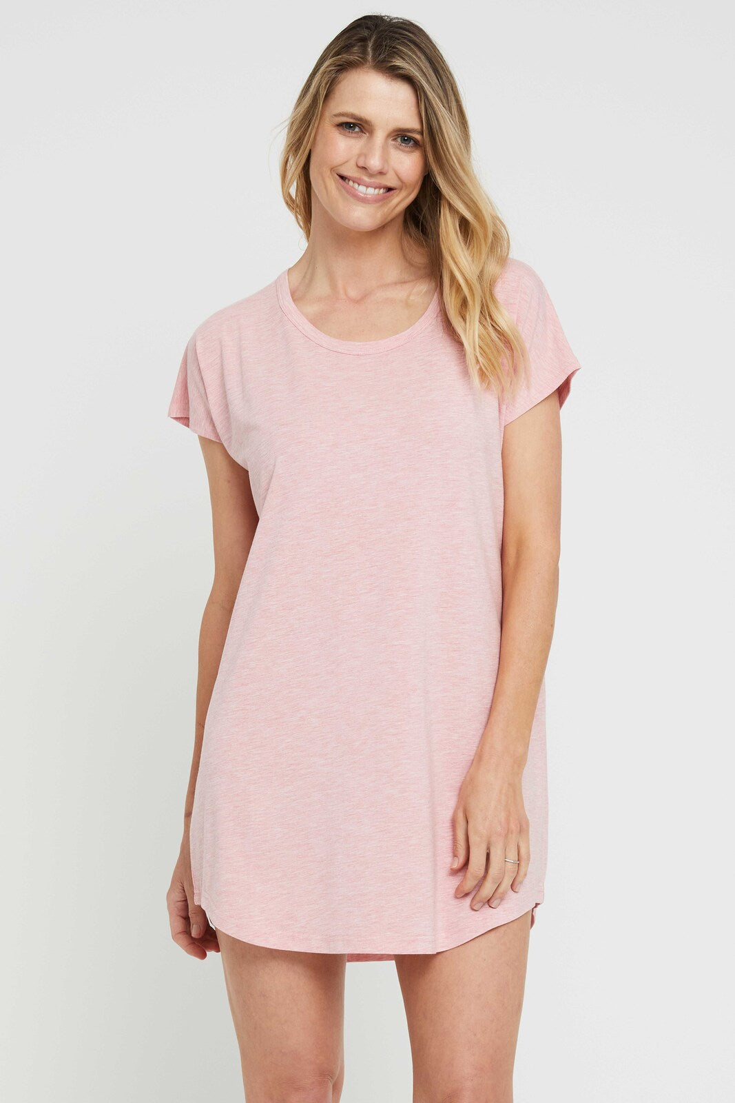 A woman wearing a pink night dress with a scoop neckline, short sleeves, and an oversized fit that falls above knee length.
