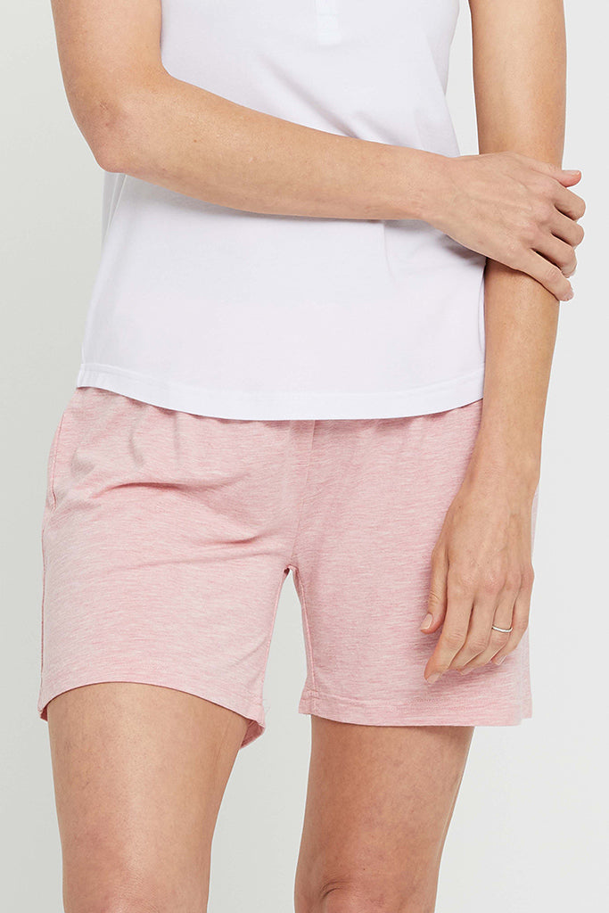 Woman wearing a white top and pink relax PJ shorts, standing against a plain background.
