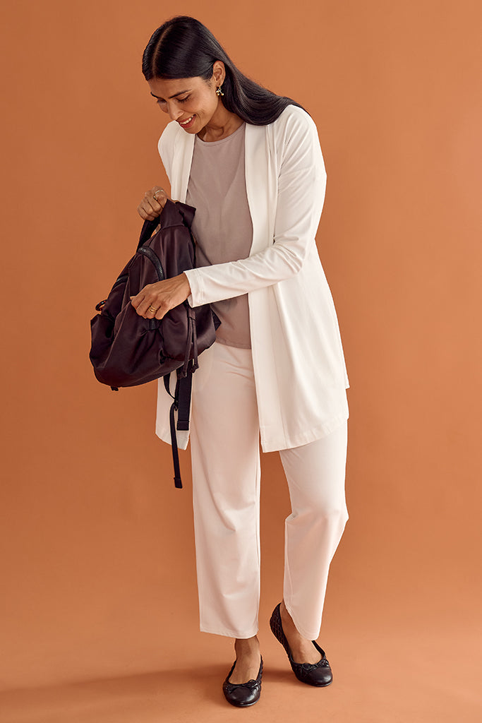 Woman in a matching white cardigan and pant holding a black bag against an orange background