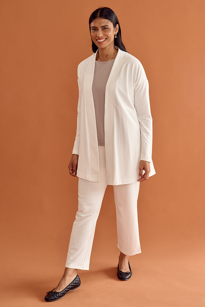 Woman wearing a white long cardigan, beige top, and pants on an orange background