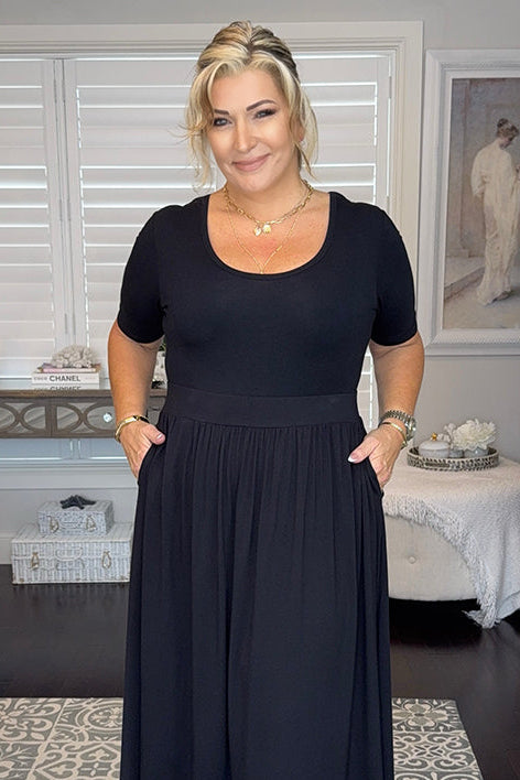 Woman wearing a black fitted tee tucked into a midi skirt, standing in a room with decor elements.