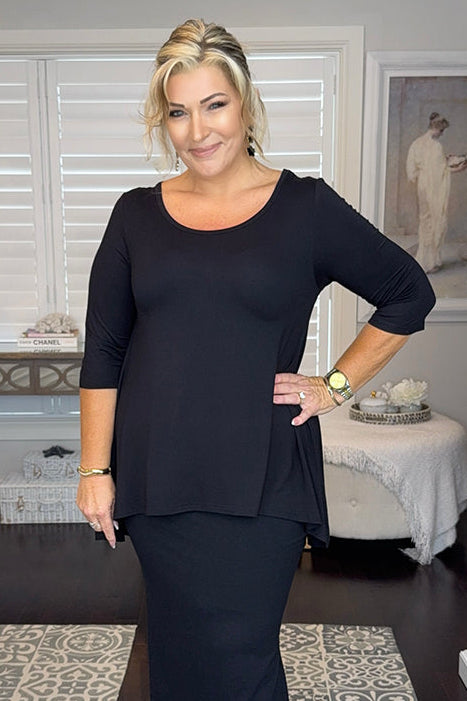 Woman wearing a black relaxed tee in an indoor setting with decor elements.